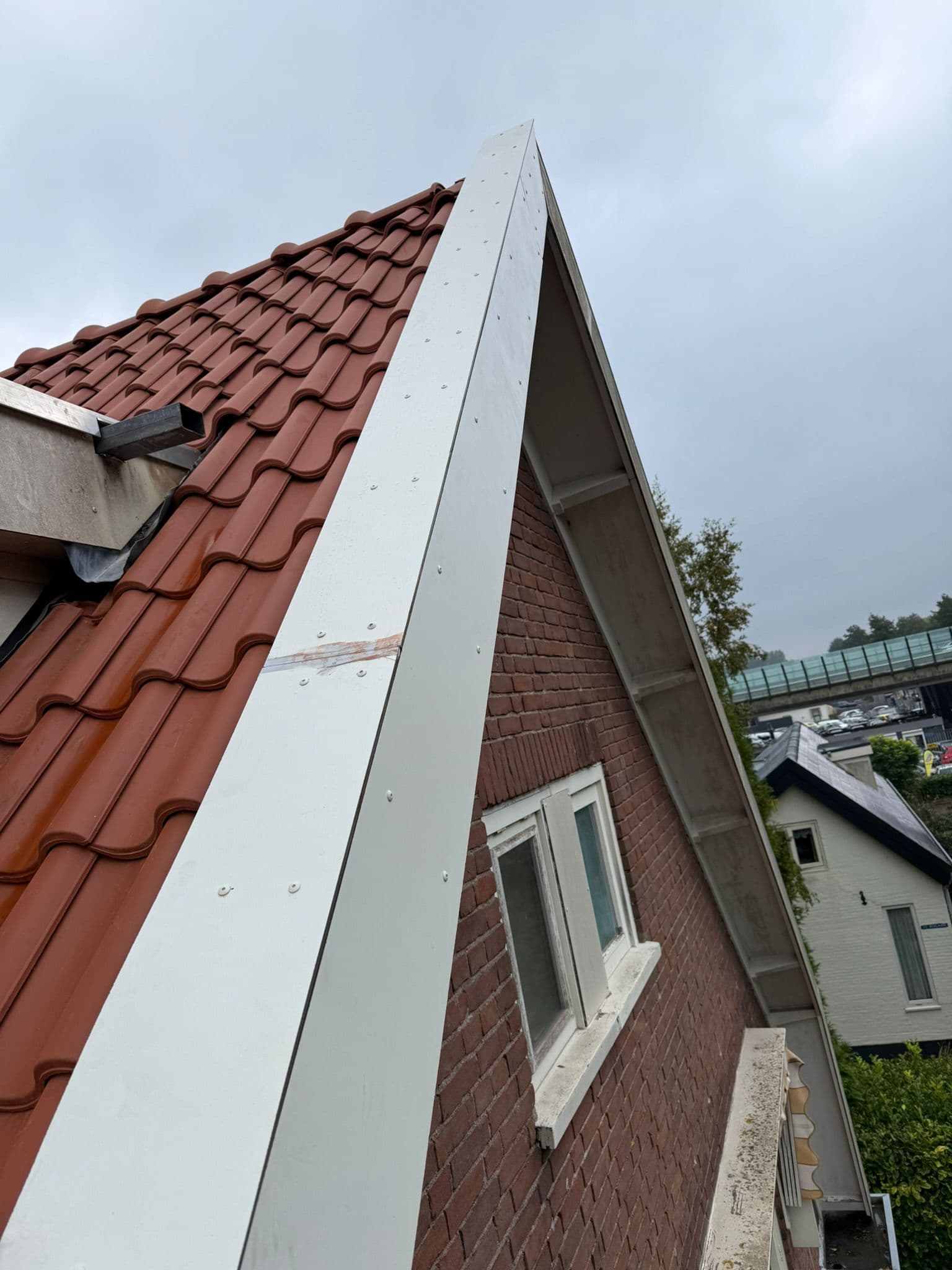 Afgewerkt zinken boeideel langs de gevel van een woning met rode dakpannen