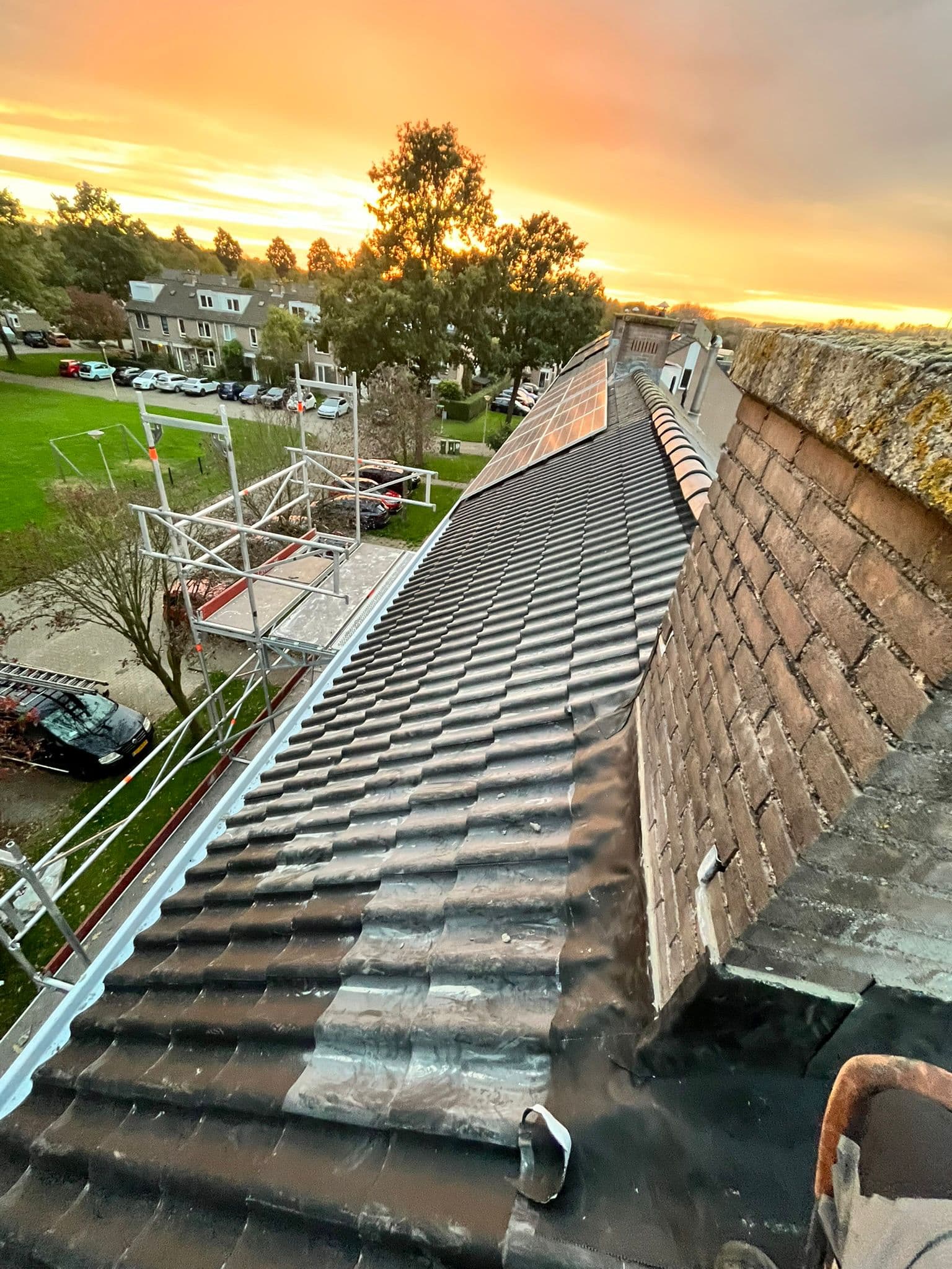 Pannendak tijdens een nokrenovatie, met steiger langs de dakrand bij zonsondergang