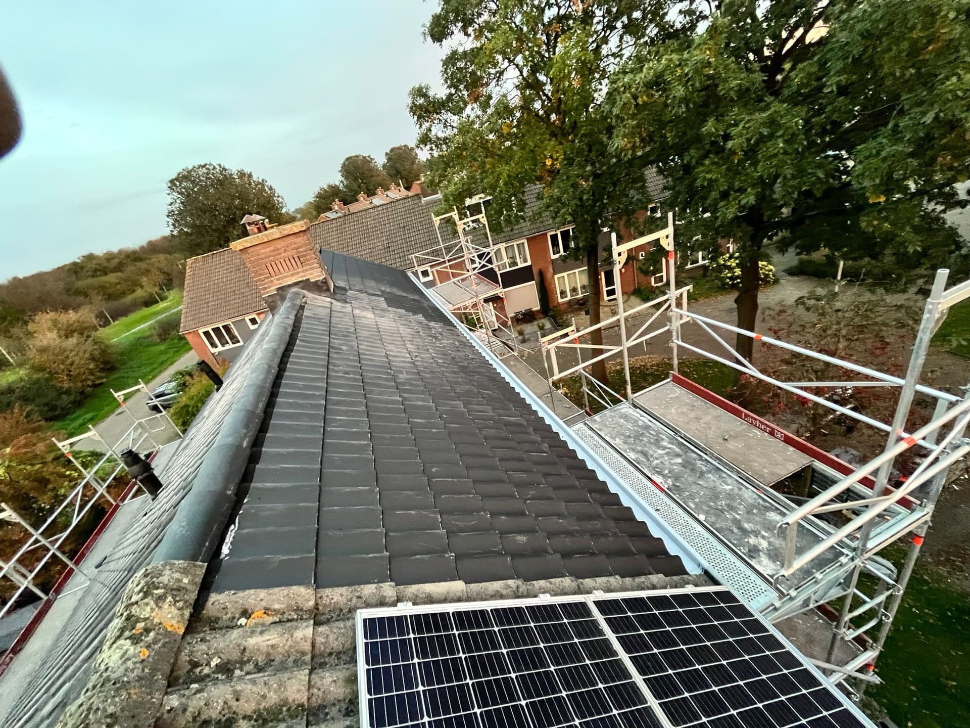 Pannendak tijdens renovatie met steiger langs de dakrand en zonnepanelen op het dakvlak